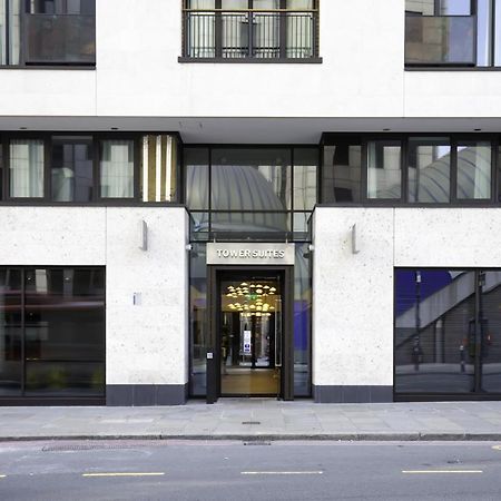 Tower Suites By Blue Orchid London Exterior photo The image shows the entrance of a modern building, characterized by its minimalist architectural design. The facade features a combination of large glass windows and smooth stone surfaces. The entrance is framed by glass doors, flanked by stylish lig