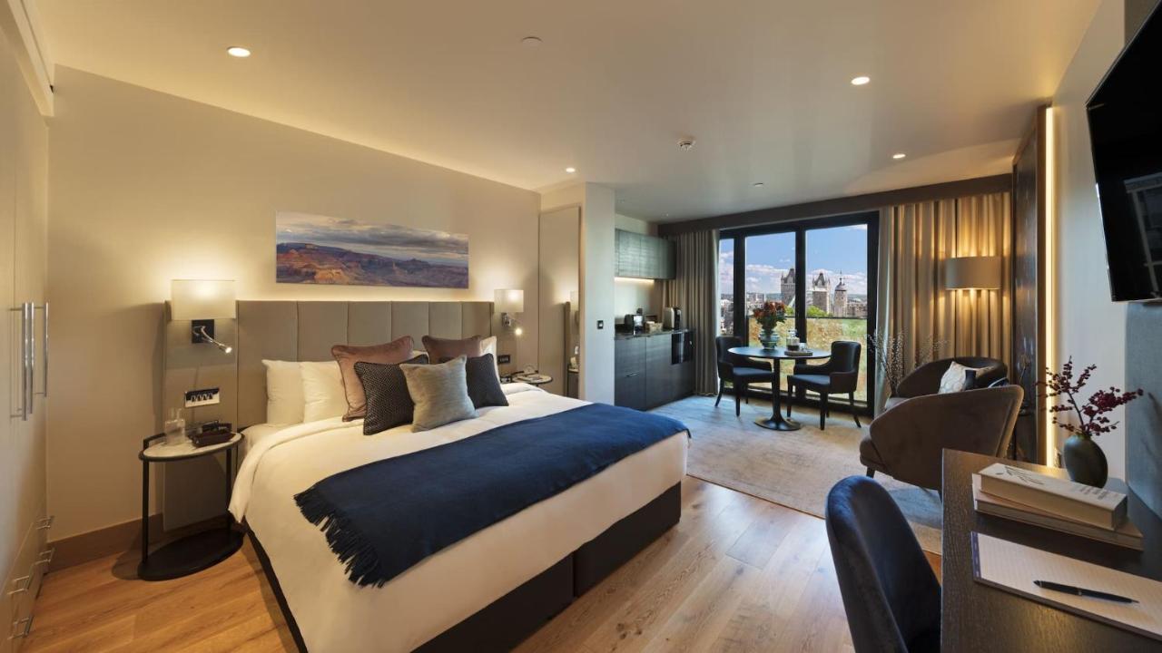 Tower Suites By Blue Orchid London Exterior photo The photo shows a modern hotel room. It features a large bed with a dark blue throw blanket and several decorative pillows. The walls are painted in neutral tones, and there's a landscape painting above the bed. To one side, there is a small kitchene