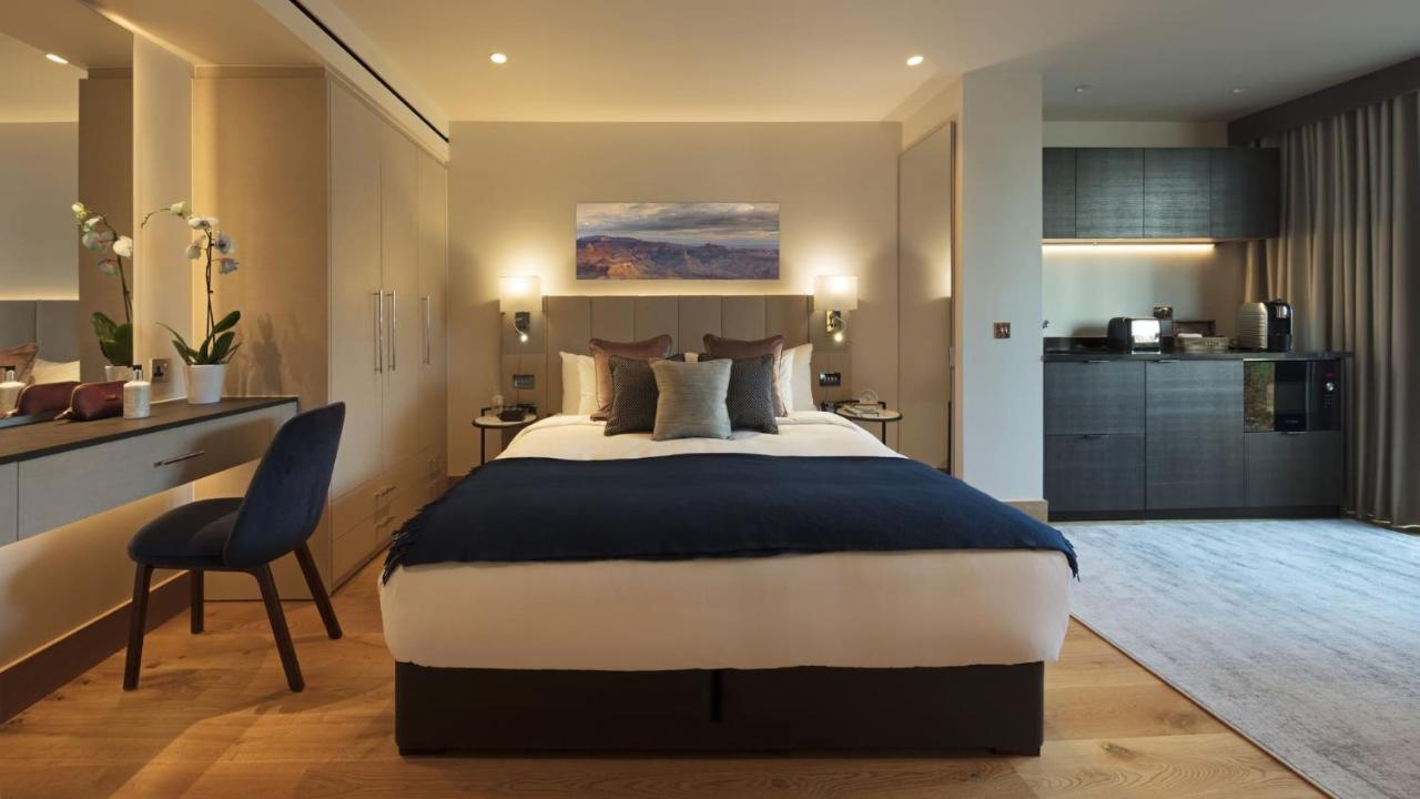 Tower Suites By Blue Orchid London Exterior photo The photo displays a modern hotel room featuring a plush bed with a dark blue bedspread and several decorative pillows. The walls are adorned in neutral tones, and there is a piece of artwork above the bed depicting a serene landscape. On the side, t