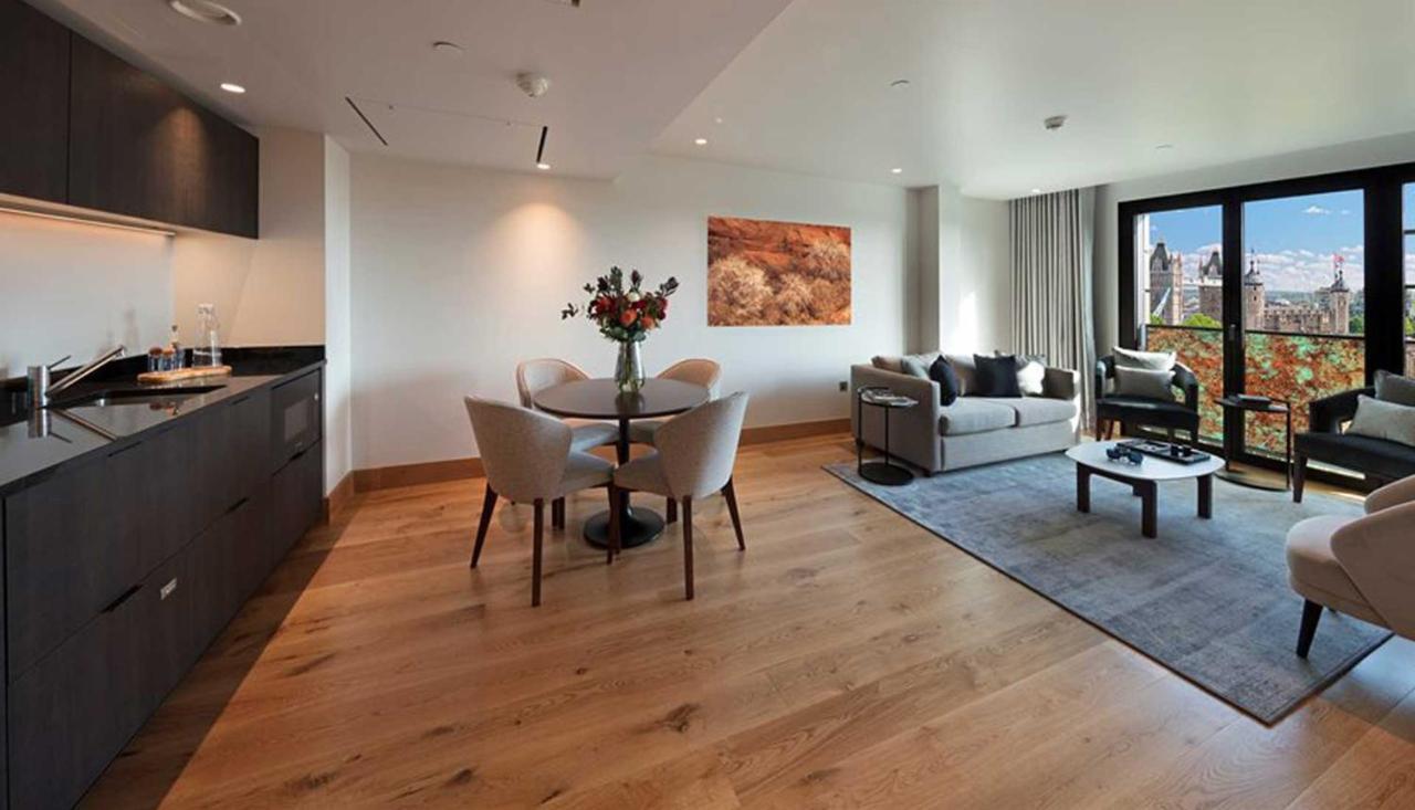 Tower Suites By Blue Orchid London Exterior photo The photo shows a modern apartment interior. On the left side, there is a kitchen area with dark cabinetry, while on the right side, a comfortable living area is visible. In the center, a round dining table is set with four chairs and a vase of flowe