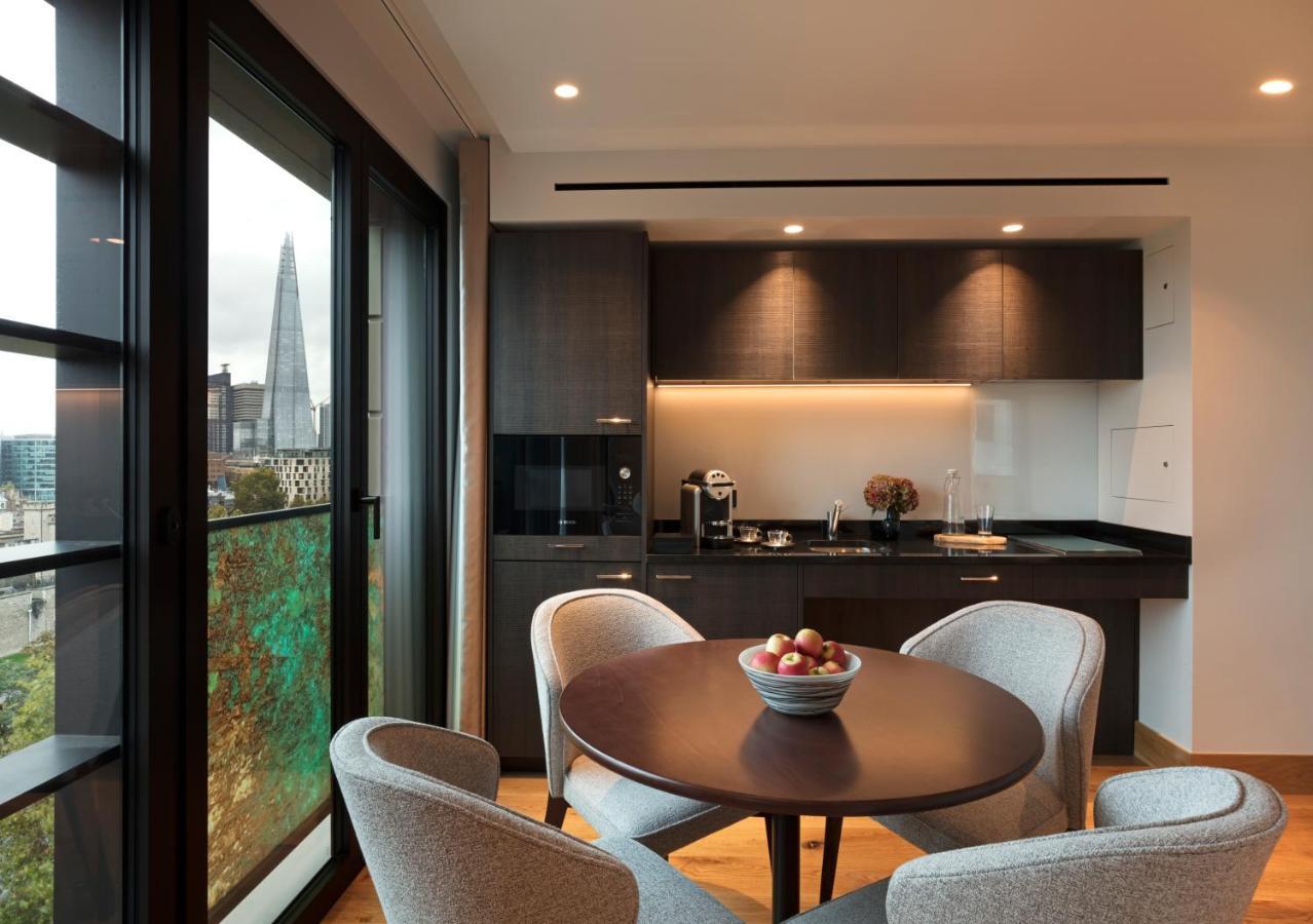 Tower Suites By Blue Orchid London Exterior photo The photo shows a modern kitchen and dining area. It features a round table with four gray chairs, and a bowl of apples is placed in the center of the table. The kitchen has dark cabinetry, a black countertop, and built-in appliances. Large windows a