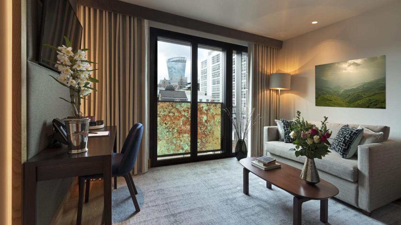 Tower Suites By Blue Orchid London Exterior photo The photo shows a modern and well-lit living space. There is a comfortable sofa with decorative cushions, a small coffee table in front of it, and a floor lamp providing additional lighting. Beside the sofa, there are decorative plants and a vase wit