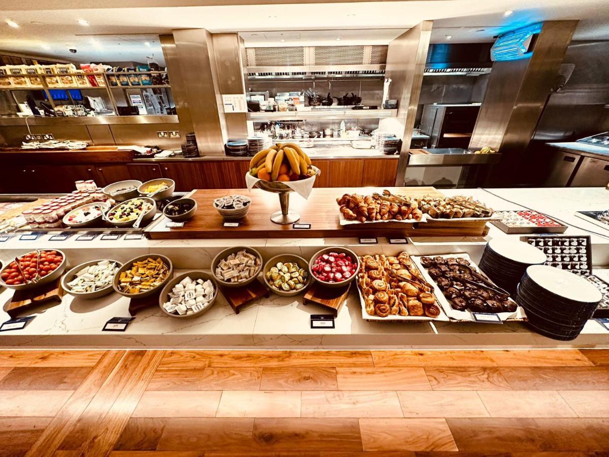 Tower Suites By Blue Orchid London Exterior photo The photo displays a beautifully arranged buffet featuring a variety of food items. There are several bowls and platters filled with colorful fruits, pastries, and desserts. In the center, a large bowl of bananas is prominently placed. Surrounding th