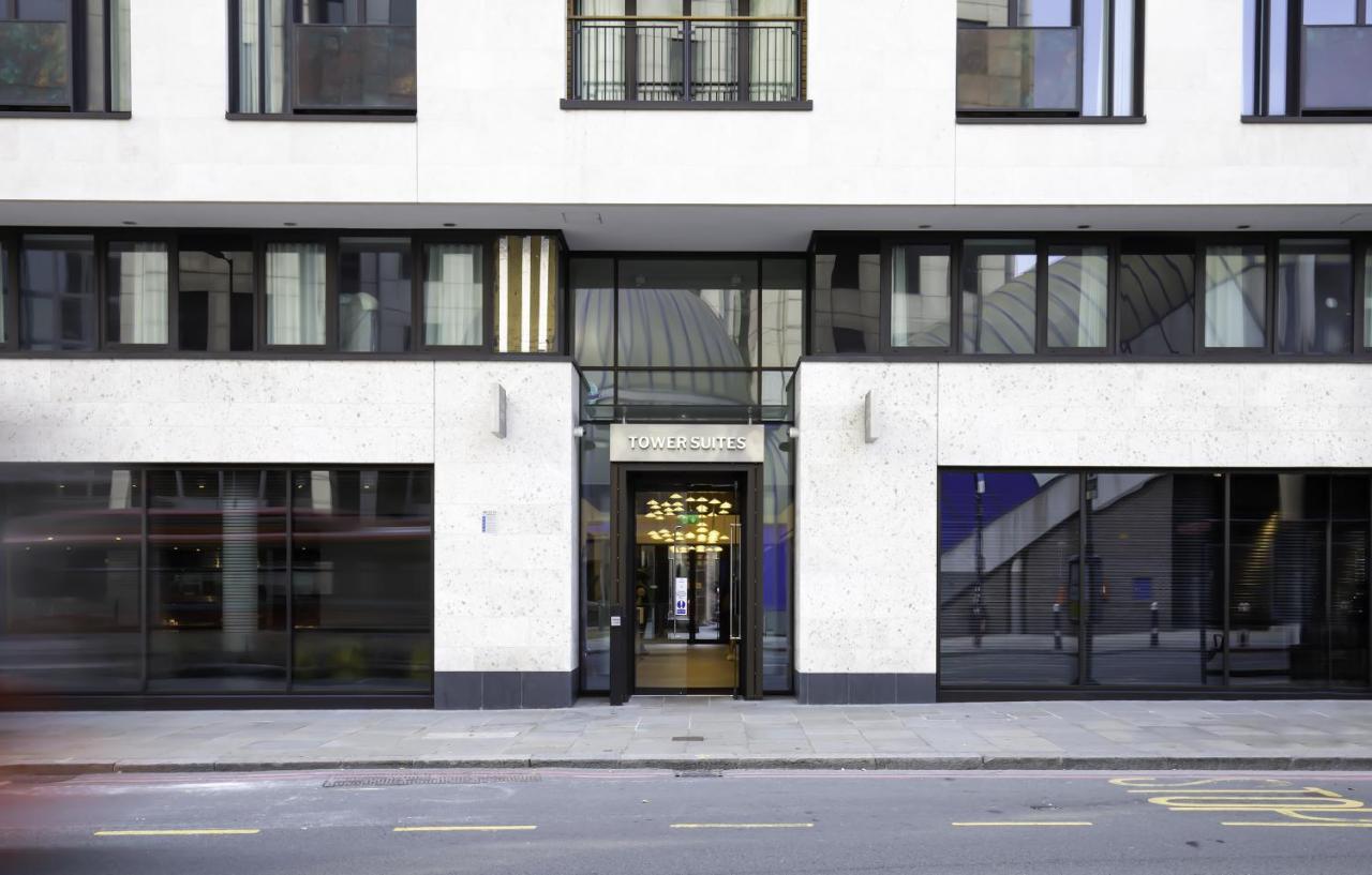 Tower Suites By Blue Orchid London Exterior photo The image shows the entrance of a modern building, characterized by its minimalist architectural design. The facade features a combination of large glass windows and smooth stone surfaces. The entrance is framed by glass doors, flanked by stylish lig